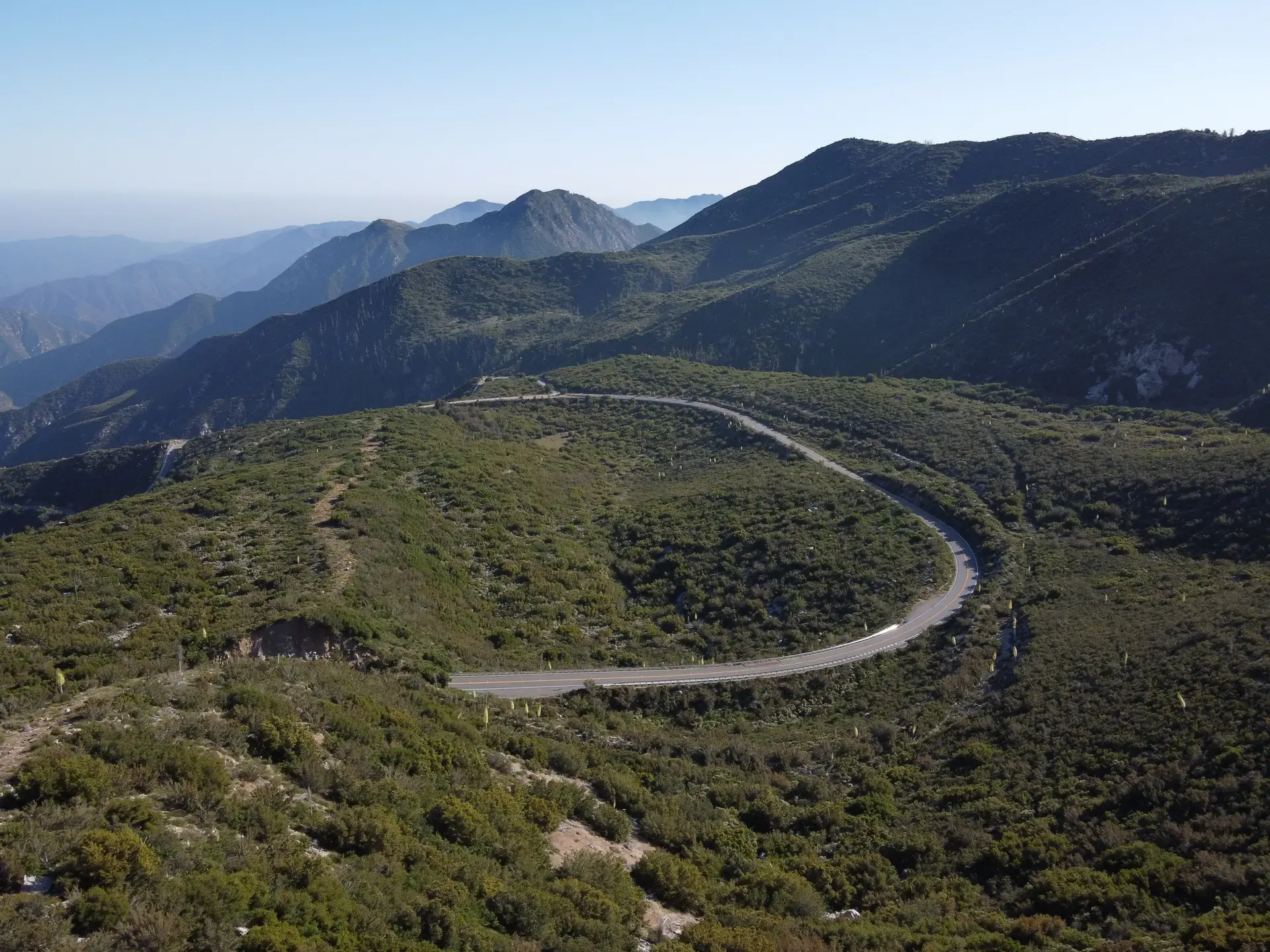 A winding road crossing green mountain ridges beneath a clear blue sky